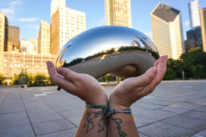 2 hands in the foreground 'holding up' the Chicago Bean in the background