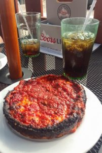 A deep dish pizza with sauce on top and a cup of coke