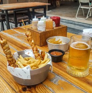 Two chicken skewer with fries and beer, with sauces in a tray behind