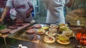 A grill full of burger patties and burger buns on a street cart flat top