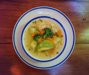 Chicken vegetable soup with broccoli and avocado in a white bowl with a blue rim