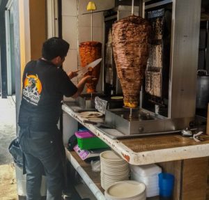 Don Sirloin employee cutting al pastor meat off of a trompo (spinning skewer of cooked meat)