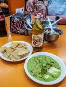 A plate of guacamole and a plate of chips, with a bottle of Sol beer