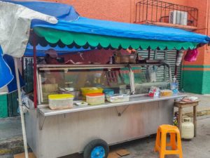 An emapanada vendor cart with a blue and green canopy and a line of toppings on the cart ledge