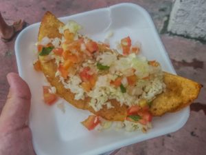 An empanada topped with cabbage, tomatoes and pico de gallo