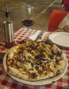Wood oven baked pizza with a crispy crust and a glass of wine on the side