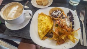 An omelette with a side of fresh cut chips, black beans and a cappuccino with a leaf design on top