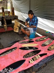 A man hand carving designs and names into wooden surfboards