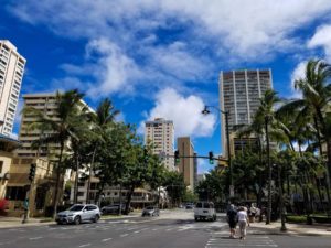 Palm tree lined streets of Honolulu with tall buildings and a bright blue sky