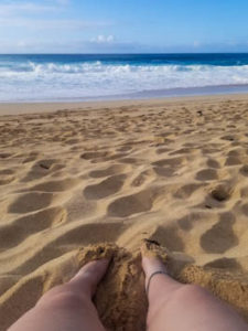 Feet in the sand with waves crashing in the background