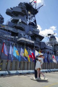 The iconic statue of the soldier kissing his girl in front of a line of flags and USS Missouri