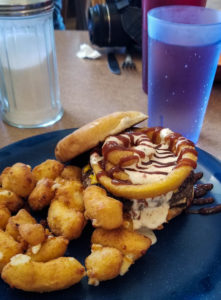 Open faced burger topped with onion rings, chipotle mayo and BBQ sauce with a side of fried cheese curds at Ekalaka Wagon Wheel in Ekalaka, Montana