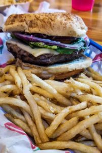 Closeup of a cheeseburger topped with pepper jack cheese, lettuce and red onion with a side of fries at Heiser's Bar and Casino in Baker, Montana