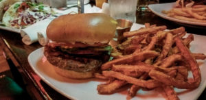 A burger topped with lettuce, tomato and onions and a side of sweet potato fries at Jake's Bar, Billings, Montana