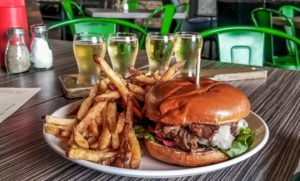 Last Chance Pub & Cider House Brisket burger with a side of fresh cut fries in front of a flight of 4 ciders