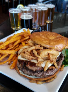 Montana Brewing Company burger topped with brisket, BBQ sauce, cheese and crispy onions. With a side of sweet potato fries and flight of 8 beers
