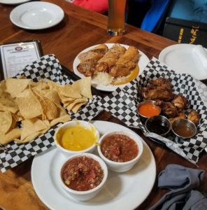 Salsa and beer cheese in small bowls with plates of chips, wings and German spring rolls at Uberbrew in Billings, Montana
