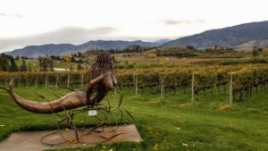 A metal mermaid sculpture overlooking a field of grape vines at Red Rooster Winery on Naramata Bench