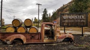 A rusted old pick up truck with 5 wine barrels in the back beside the Red Rooster Winery sign