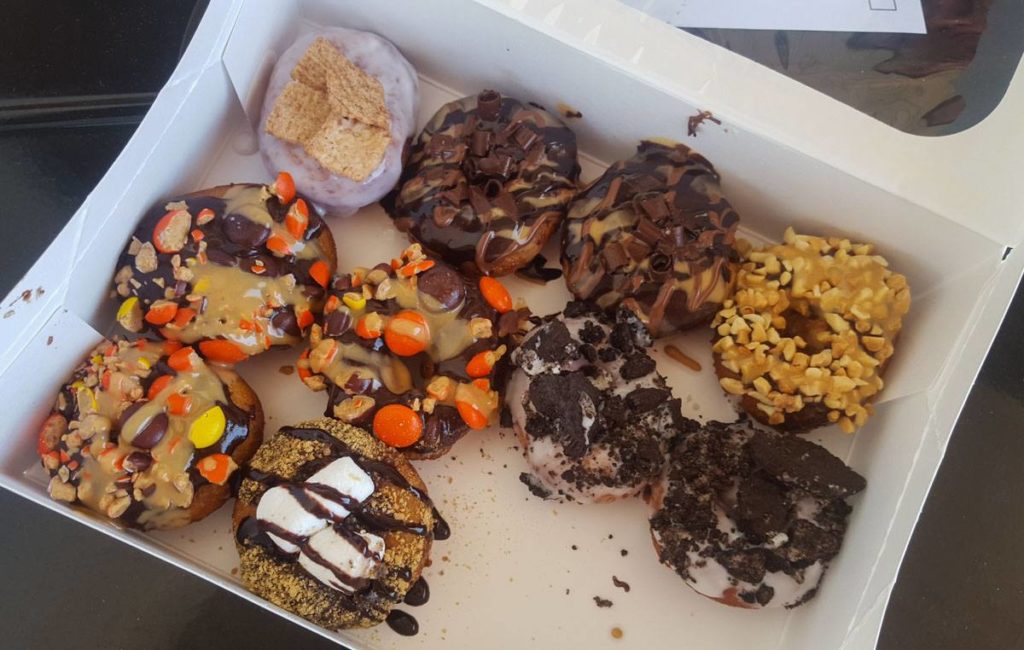 A box with 10 mini donuts inside, topped with ingredients like Oreo crumbles, Reece's Pieces, marshmallows, Cinnamon Toast Crunch cereal and chocolate and peanut butter drizzles. 