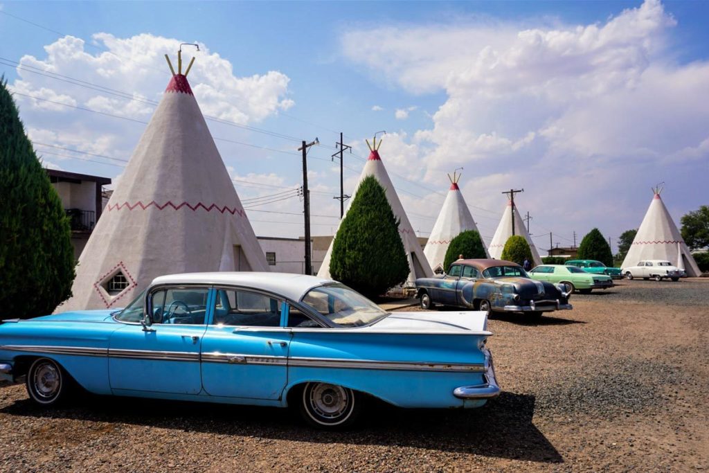 An old corvette stands in front of a line of teepees, with more old cars in the background.