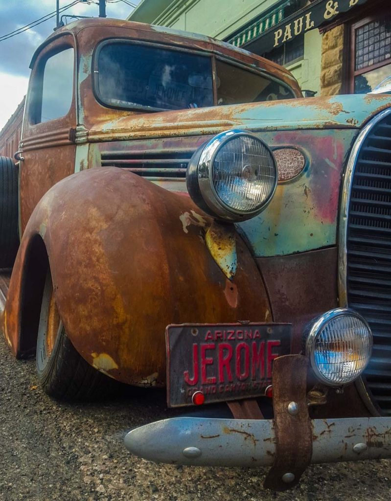 A closeup of the front passenger side bumper on an old Ford truck with a license plate with 'Jerome' on it. 