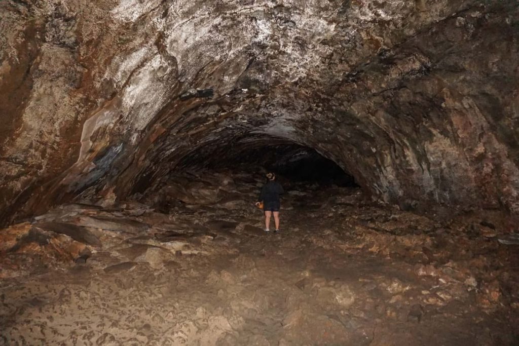 A dark cave with a woman standing in the distance with her back to the camera