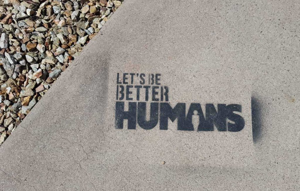 'Let's be better humans' painted on a sidewalk in black paint