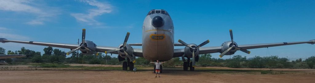 A boy standing under the nose of a plane with his arms outstretched, showing how big the wingspan of the plane is