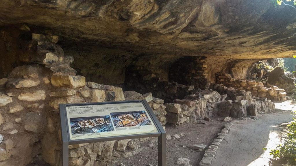 Rocks piled up to form walls at the outside of the cave dwellings with an informational sign in front. 
