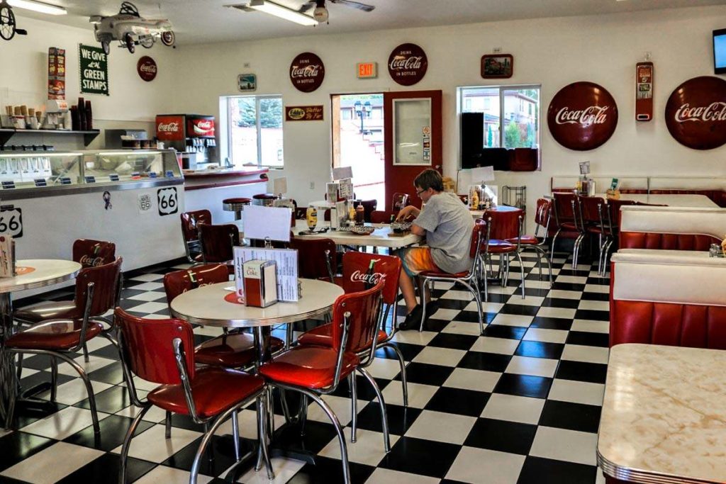 A 1950's style diner with black & white checkered floors, red chairs, white tables and Coca Cola decor
